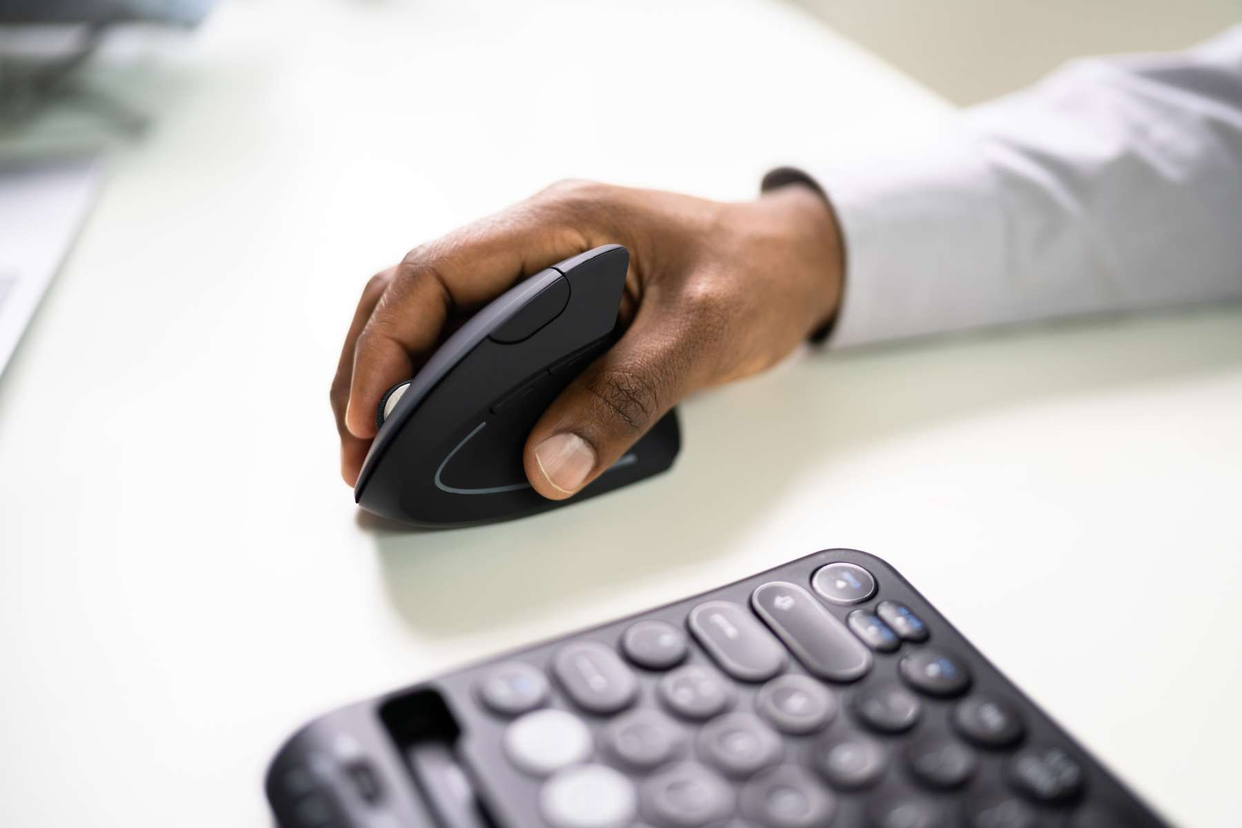Eine Hand führt eine ergonomische Maus auf einem Schreibtisch neben einer Tastatur.