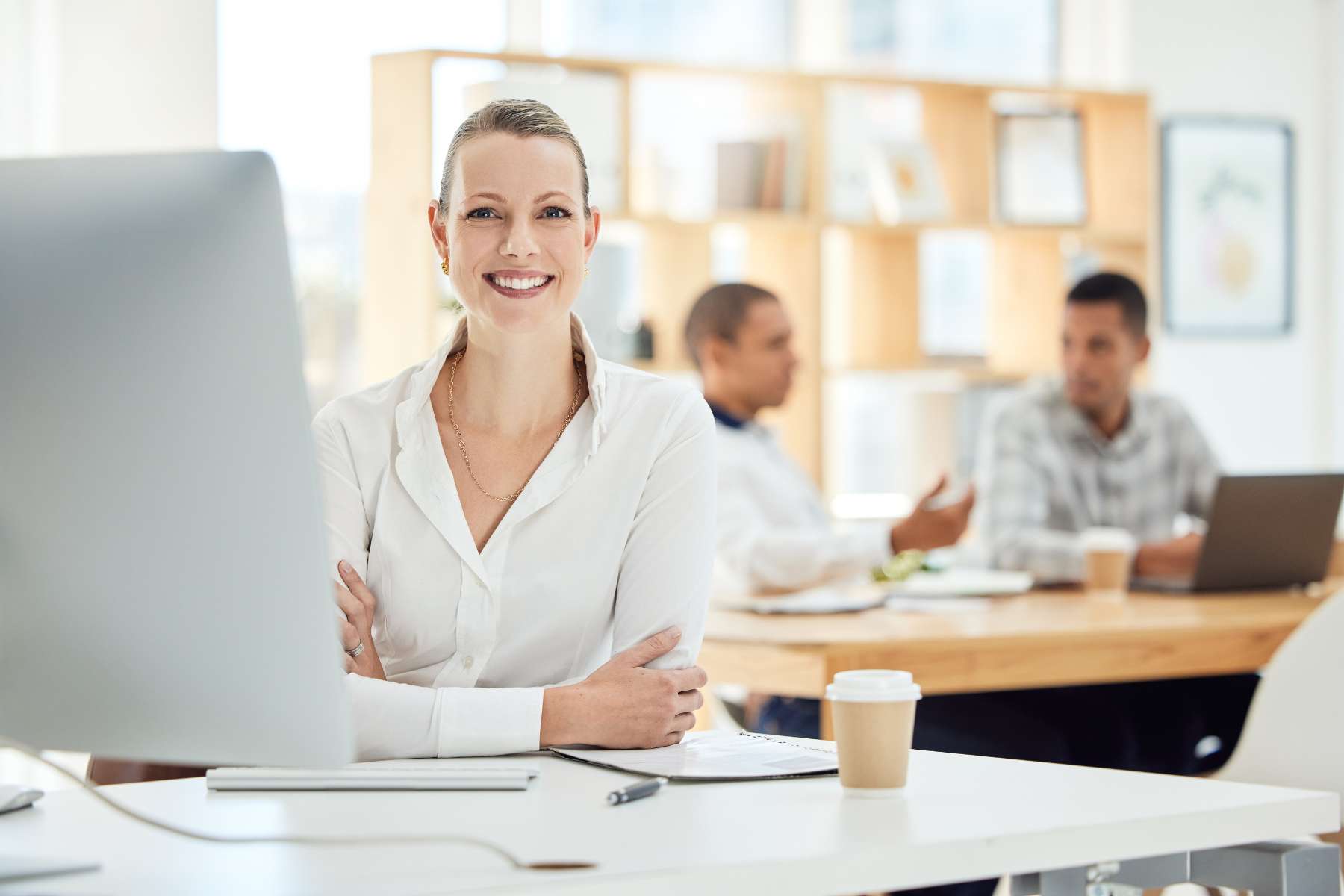 Eine lächelnde junge Frau sitzt am Schreibtisch in einem Büro.