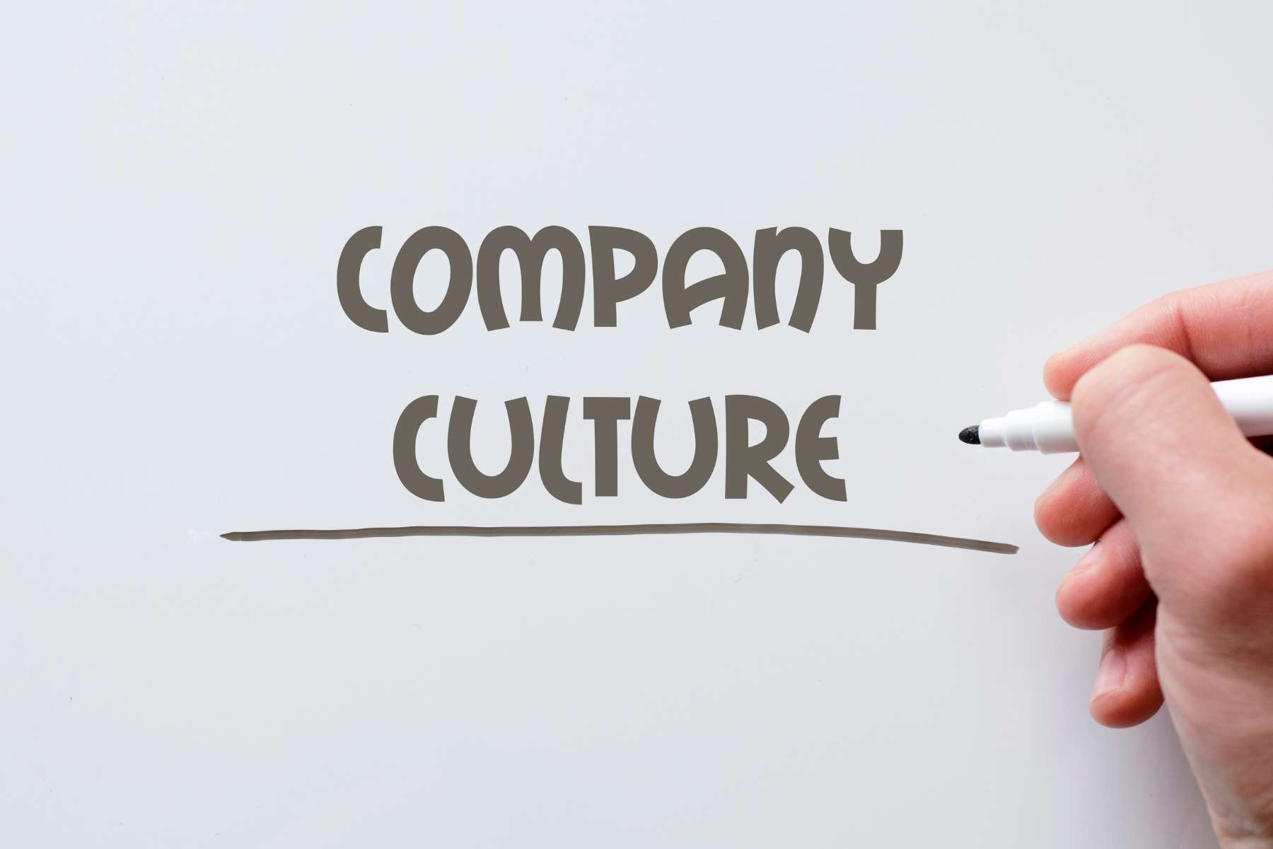 Nahaufnahme einer Hand, die einen Stift hält, mit dem groß die Worte Company Culture auf eine weiße Tafel geschrieben worden sind.