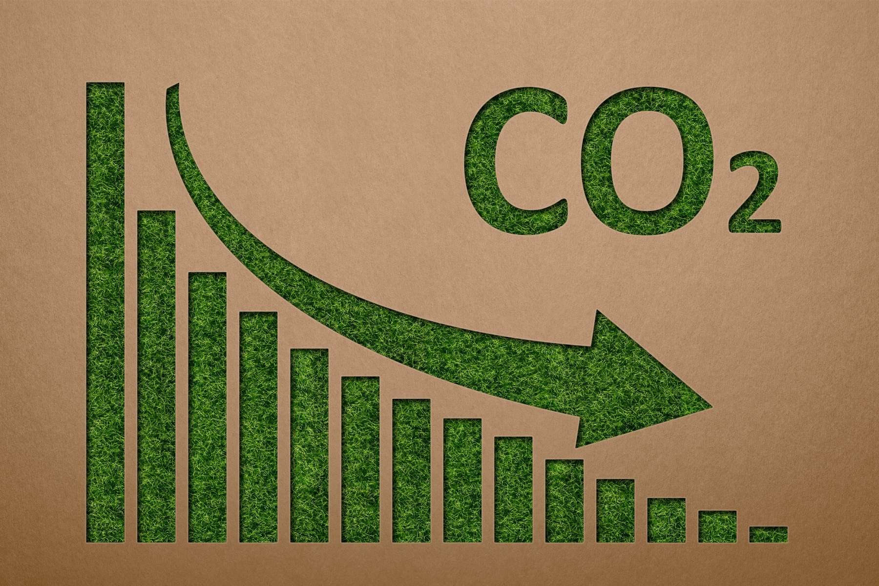 Auf einem Kunstrasenstück liegt eine Holzschablone, mithilfe welcher ein sinkender CO2 Wert grafisch dargestellt wird, als Ziel kreislauffähiger Büros.