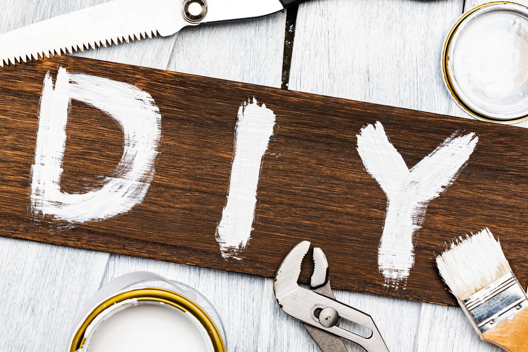 Holzschild auf das mit weißer Schrift das Wort DIY gemalt wurde und das von Werkzeugen umrandet ist.