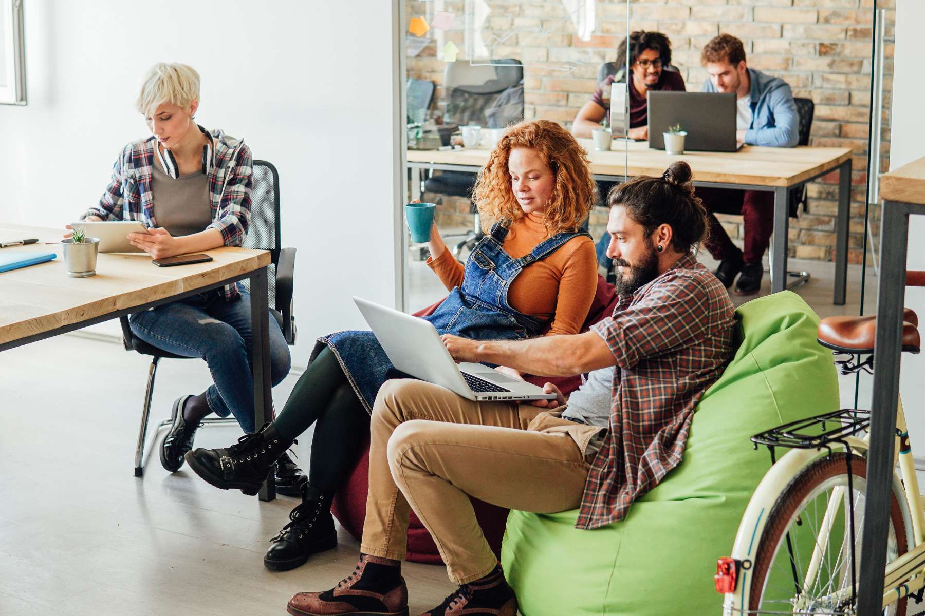 Co-Working Space Büro. in dem mehrere Mitarbeiter in verschiedenen Bereichen an Laptops und Tablets arbeiten und teilweise auf Sitzsäcken sitzen.