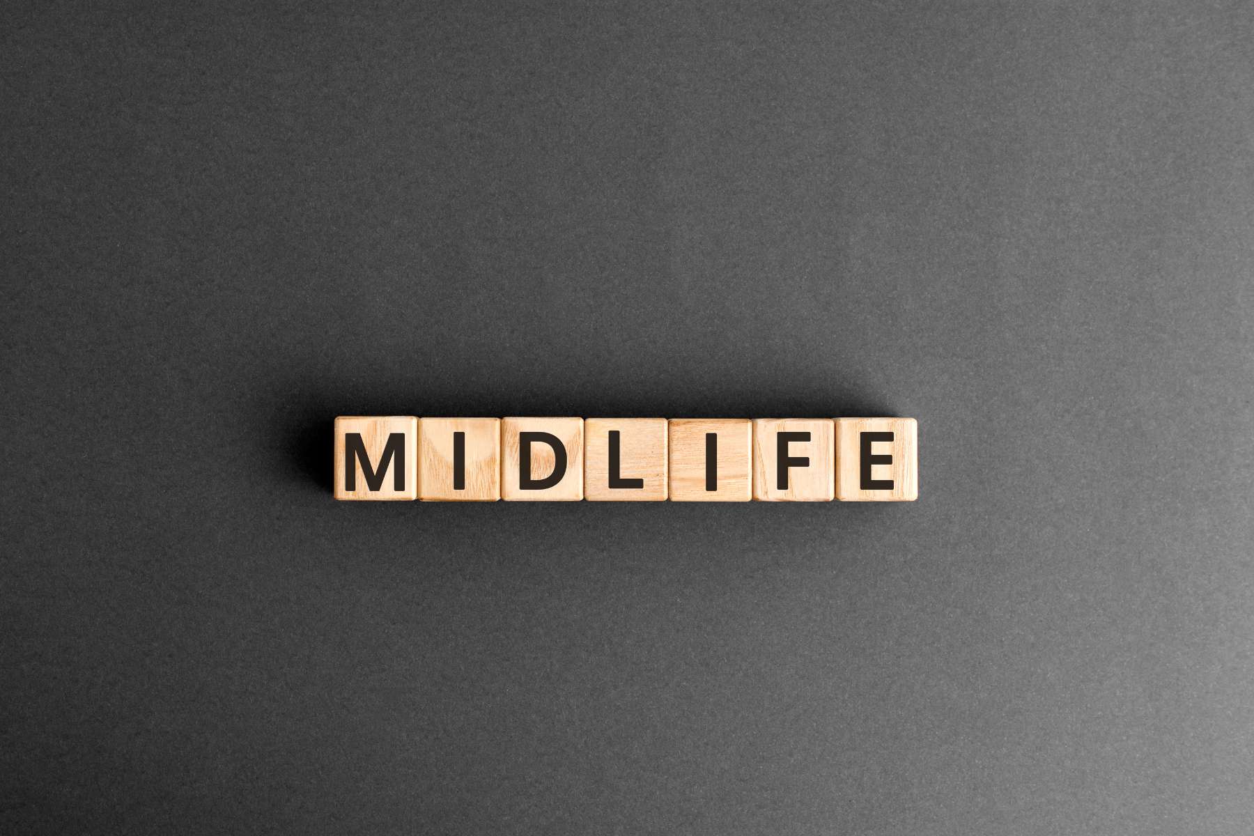 Das Wort Midlife ist auf Holzwürfeln abgebildet, welche auf einem schwarzen Untergrund liegen.