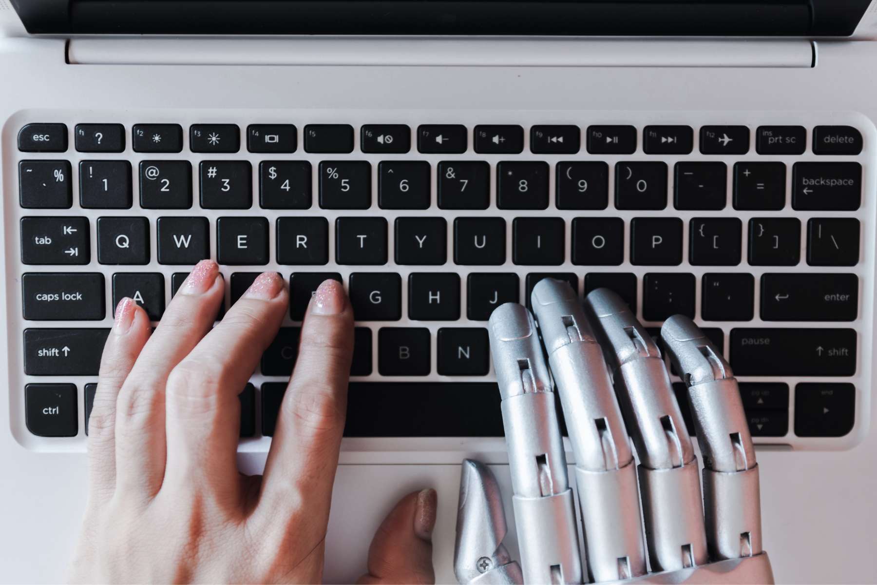 Ein Laptop, an dessen Tastatur eine menschliche Hand und eine Roboterhand arbeiten, als Sinnbild für KI-gesteuerte Unterstützung beim Thema Microlearning im Büro.