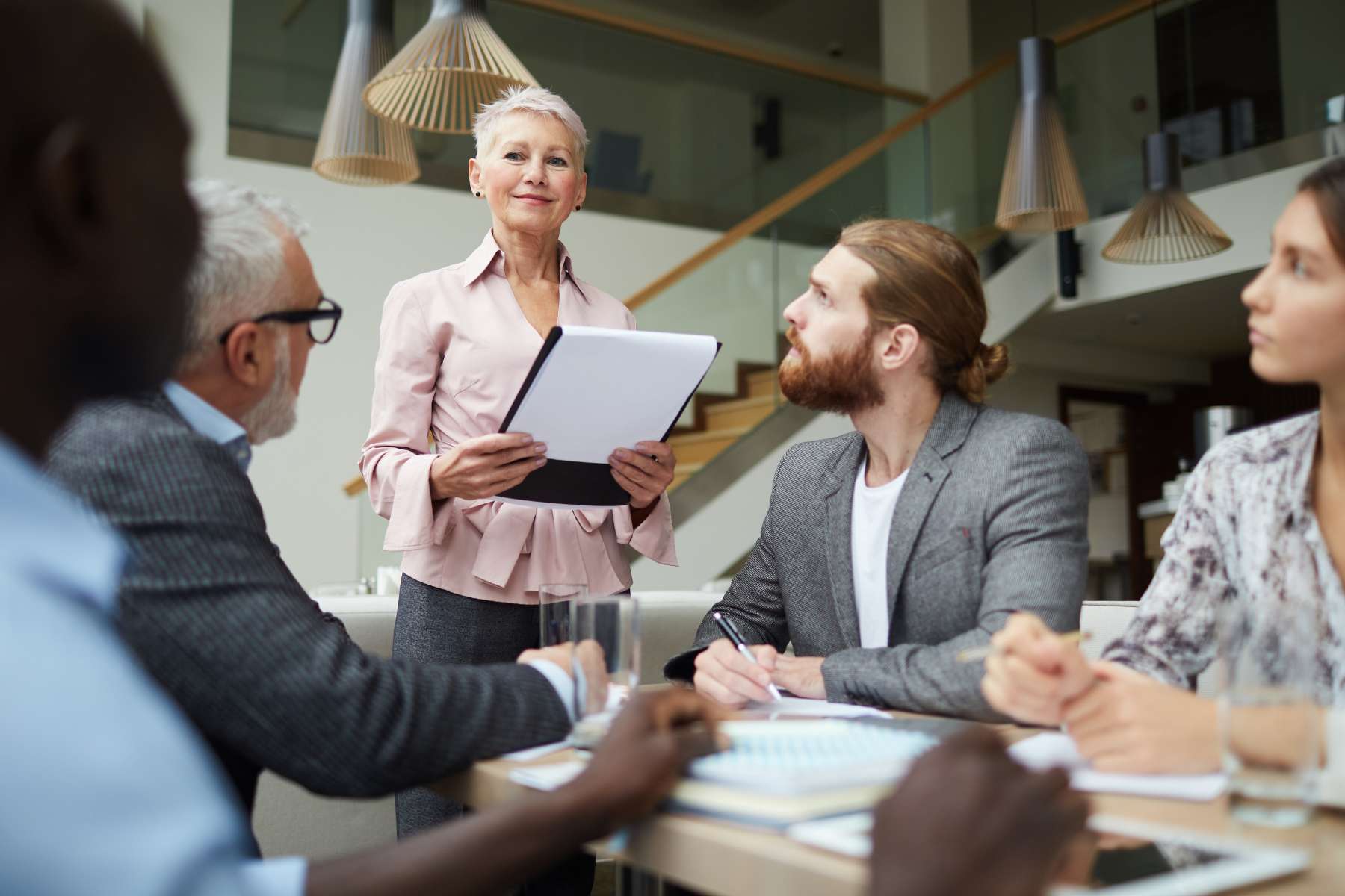 Eine Gruppe von vier Büroangestellten sitzt an einem Tisch und blickt zu ihrer lächelnden Chefin auf, die gerade etwas zum Thema Microlearning im Büro erzählt.
