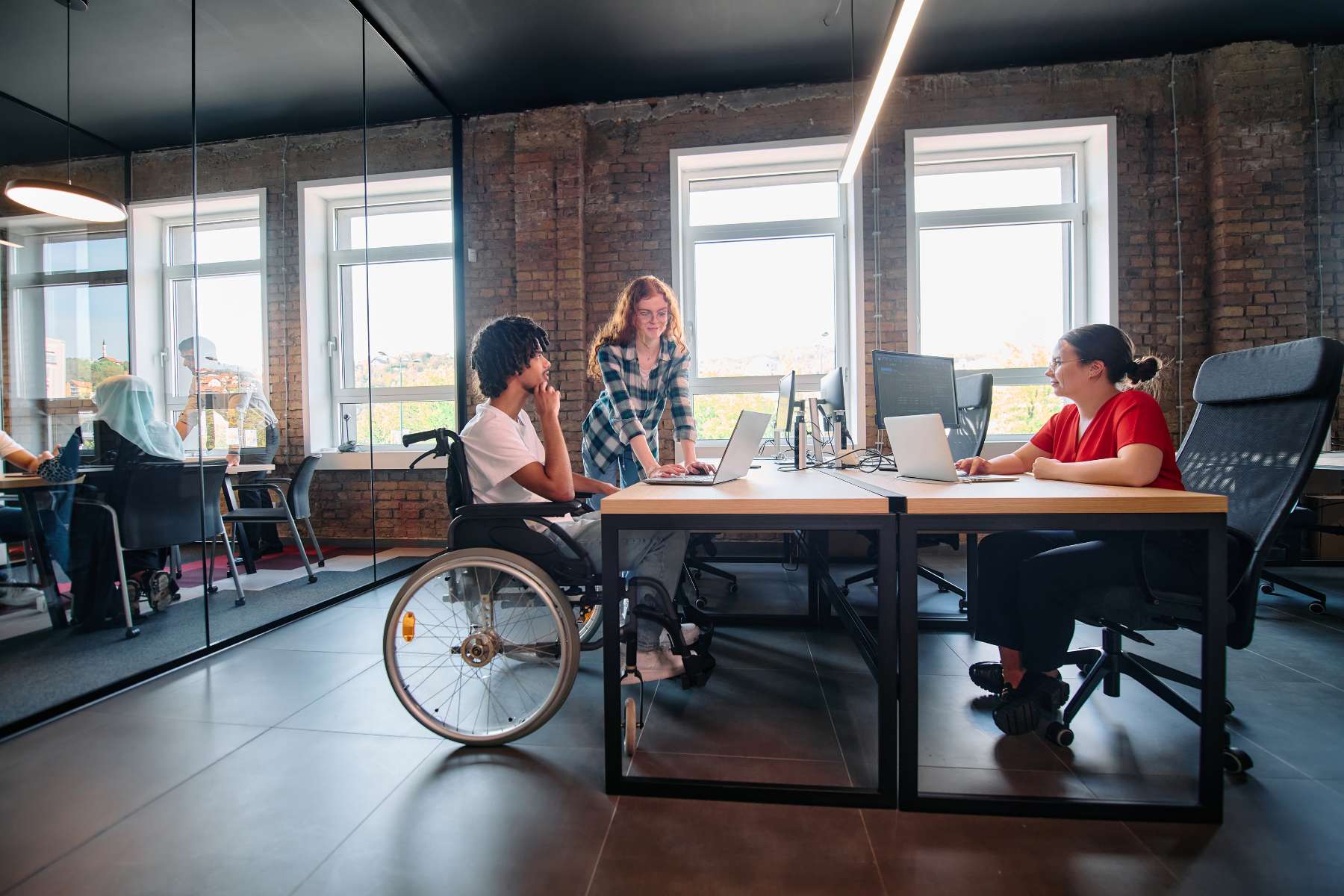 Eine Gruppe junger Angestellter, darunter ein Mann im Rollstuhl, sitzt bzw. steht im Büro und unterhält sich als Sinnbild neurodivergenter Arbeitswelten.