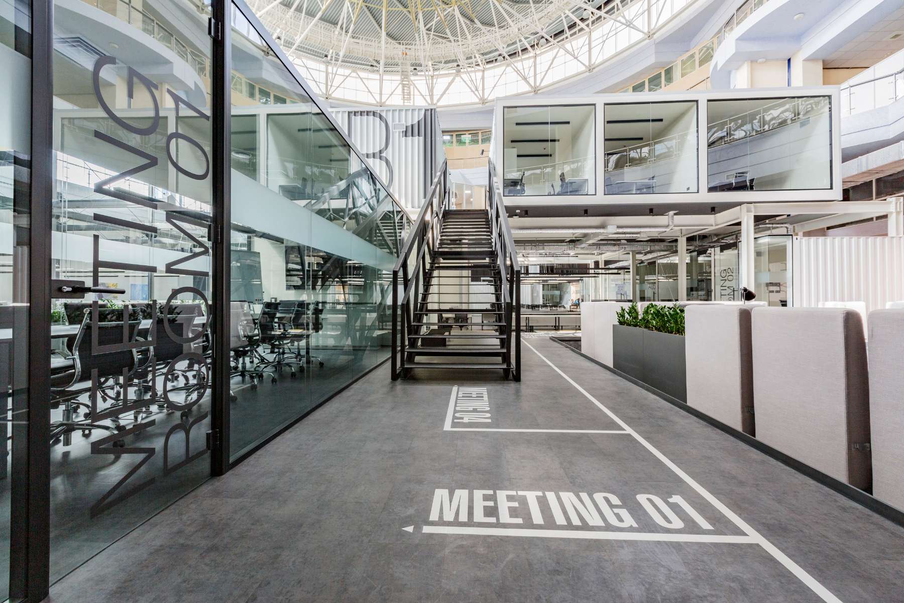 Modernes und weitläufiges New Work Büro im Loft-Stil mit Meetingraum, Loungebereich und erhöhten Bürokabinen.