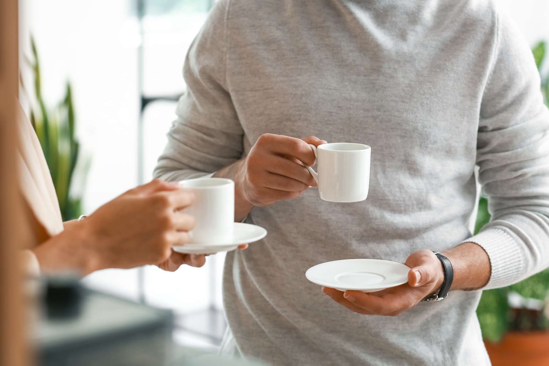 Eine Frau und ein Mann, von denen man je nur den Oberkörper sieht, stehen im Büro und unterhalten sich bei einer Tasse Kaffee, als Sinnbild zum Thema Return to Office.